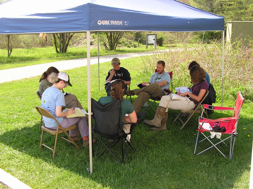 Seven people sit under a canopy with copies of Pyle open on their laps.